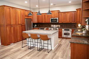 Kitchen featuring open shelves, wood finish cabinetry, decorative light fixtures, stainless steel appliances, and a breakfast bar area.