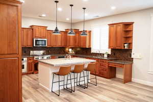 Kitchen featuring wood finish cabinets, dark stone counters, a breakfast bar, pendant lighting, and stainless steel appliances.