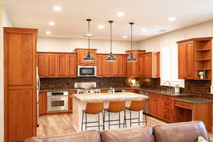 Kitchen featuring wood finish cabinets, stainless steel appliances, pendant lighting, open shelves, and a breakfast bar.
