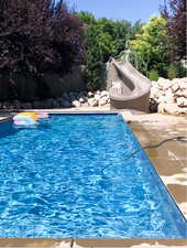 Picture Summer 2025. View of pool with a water slide and a fenced backyard.