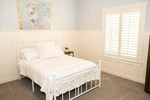 2nd main floor bedroom with a decorative wall, wainscoting, carpet.