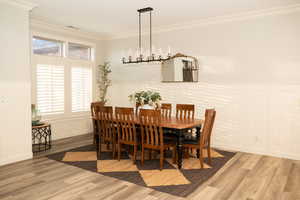 Dining area featuring wainscoting, a decorative wall, ornamental molding, lvp radiant flooring and hanging lights.