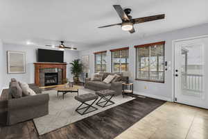 Living room featuring light wood-style floors, ceiling fan, and a tiled fireplace