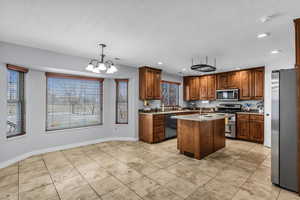 Kitchen featuring stainless steel appliances, an island with sink, wood finish cabinetry, hanging lights, and light countertops
