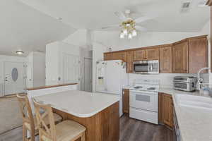 Kitchen featuring a breakfast bar, vaulted ceiling, stainless steel appliances, wood finish cabinetry, and light countertops