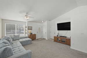 Carpeted living area with vaulted ceiling and ceiling fan