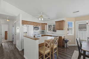 Kitchen with light countertops, stainless steel appliances, a breakfast bar area, dark wood-type flooring, and vaulted ceiling
