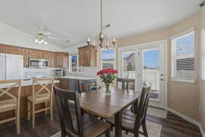 Dining area with a chandelier, vaulted ceiling, dark wood-style floors, and ceiling fan