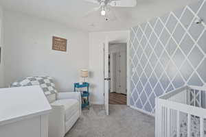 Carpeted bedroom with an accent wall, a nursery area, ceiling fan, and wallpapered walls