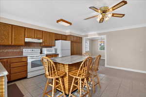 Kitchen featuring white appliances, a breakfast bar, wood finish cabinetry, a ceiling fan, and tasteful backsplash