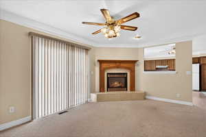 Unfurnished living room with carpet floors, a warm lit fireplace, a ceiling fan, and ornamental molding