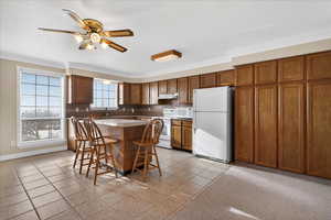 Kitchen with white appliances, a ceiling fan, crown molding, wood finish cabinetry, and a center island