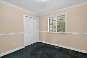 Unfurnished bedroom featuring dark carpet, a closet, a textured ceiling, and crown molding