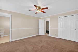 Unfurnished bedroom featuring carpet, a ceiling fan, a closet, ornamental molding, and connected bathroom