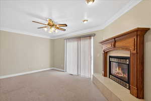 Unfurnished living room featuring ornamental molding, carpet floors, a tiled fireplace, and a ceiling fan