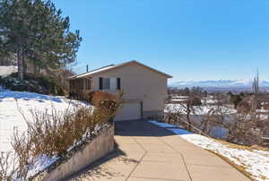 View of snow covered exterior with an attached garage, concrete driveway, and a mountain view