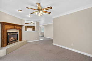 Unfurnished living room featuring ornamental molding, carpet floors, a fireplace, and ceiling fan