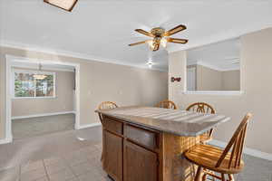 Kitchen with a kitchen bar, light carpet, light tile patterned floors, light stone countertops, and crown molding