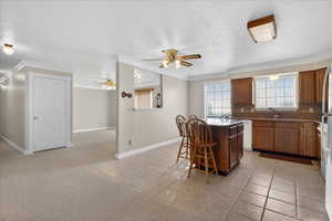 Kitchen featuring a breakfast bar, light colored carpet, a ceiling fan, a kitchen island, and ornamental molding