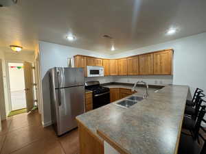 Kitchen featuring stainless steel appliances, dark countertops, a breakfast bar area, a peninsula, and wood finish cabinets