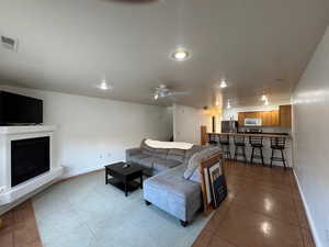 Living area featuring a ceiling fan, a fireplace with raised hearth, light tile patterned flooring, and recessed lighting