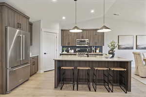 Kitchen featuring stainless steel appliances, decorative light fixtures, a center island with sink, light stone counters, and a breakfast bar area