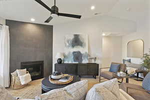Living area featuring vaulted ceiling, ceiling fan, recessed lighting, a tiled fireplace, and wood finished floors