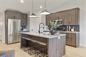 Kitchen with stainless steel appliances, a breakfast bar, tasteful backsplash, pendant lighting, and a kitchen island with sink