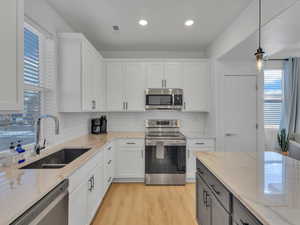 Dual tone kitchen featuring stainless steel appliances, light stone countertops, pendant lighting, two tone cabinetry, and light wood-style flooring