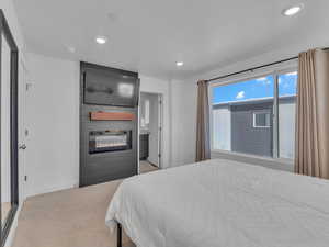 Bedroom with a large fireplace, light colored carpet, recessed lighting, and ensuite bath