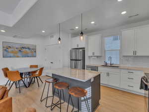 Kitchen featuring light stone countertops, hanging light fixtures, light wood-type flooring, two tone color scheme, and stainless steel appliances