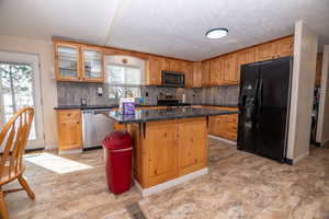 Kitchen with stainless steel appliances, backsplash, a kitchen island, a kitchen breakfast bar, and dark stone countertops