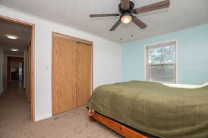 Carpeted bedroom with a textured ceiling, a closet, and a ceiling fan