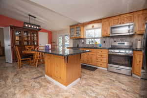 Kitchen featuring stainless steel appliances, vaulted ceiling, decorative backsplash, a center island, and glass fronted cabinets