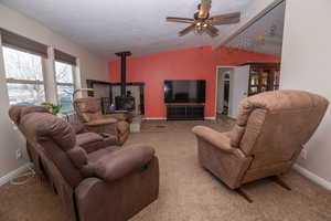 Carpeted living area with a wood stove, a ceiling fan, and beamed ceiling