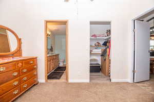 Bedroom with ensuite bath, light colored carpet, and a walk in closet