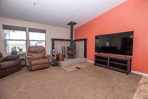 Carpeted living area with lofted ceiling and a wood stove