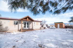 Snow covered rear of property with french doors, a storage shed, a wooden deck, and a metal roof