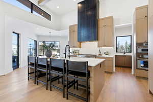 Kitchen with light wood finish cabinetry, a breakfast bar, light wood finished floors, a kitchen island with sink, and decorative light fixtures