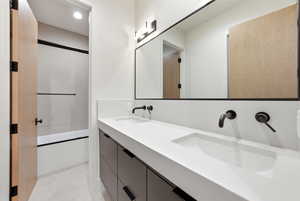 Full bath with combined bath / shower with glass door, double vanity, and light flooring