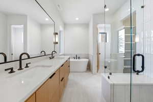 Full bath featuring double vanity, a shower stall, light tile patterned floors, a wainscoted wall, and tile walls