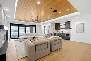 Living area with a wooden tray ceiling, wet bar, light wood-type flooring, beverage cooler, and a stone fireplace