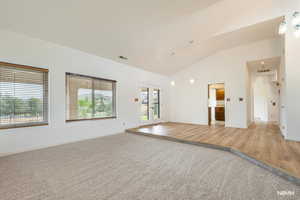 Unfurnished room featuring french doors, arched walkways, light colored carpet, vaulted ceiling, and light wood finished floors