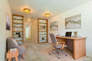 Office featuring a textured ceiling, light wood finished floors, and built in shelves