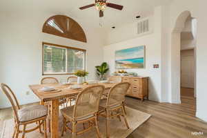 Dining space with light wood-type flooring, a ceiling fan, a high ceiling, and arched walkways