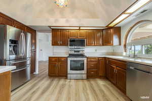 Kitchen with stainless steel appliances, light countertops, vaulted ceiling, light wood-style floors, and wood finish cabinets