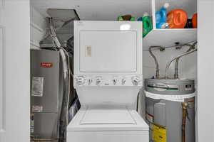 Laundry area with stacked washer / dryer, strapped water heater, and heating unit
