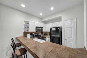 Kitchen featuring white cabinetry, freestanding refrigerator, open shelves, tasteful backsplash, and stainless steel electric stove