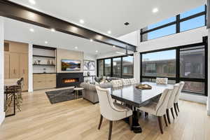 Dining space featuring a fireplace, light wood-style floors, recessed lighting, ceiling fan, and a high ceiling