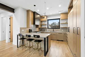 Kitchen featuring light wood finish cabinets, open shelves, a kitchen breakfast bar, a peninsula, and light wood finished floors